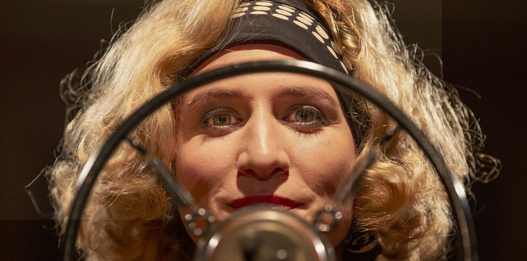 Close-up in The Soundman (2025) of a woman framed by a radio microphone and pop filter under warm studio lights.